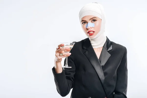 Mulher elegante com ligaduras sobre a cabeça após cirurgia plástica segurando vidro com coquetel isolado no branco — Fotografia de Stock
