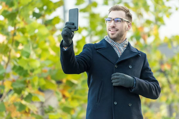 Alegre hombre tomando selfie con borrosa verde árbol - foto de stock