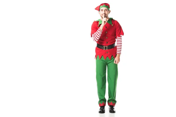 Sonriente hombre en traje de elfo de Navidad mostrando silencio signo de silencio y mirando a la cámara aislada en blanco - foto de stock