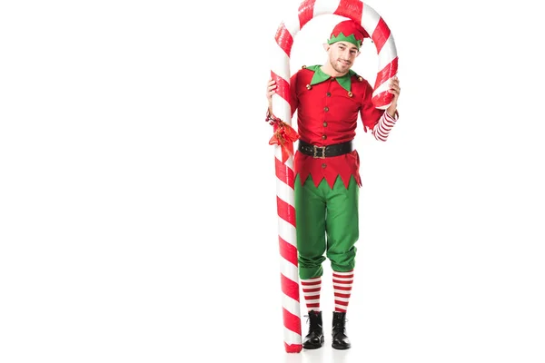 Man in christmas elf costume standing under big candy cane isolated on white — Stock Photo