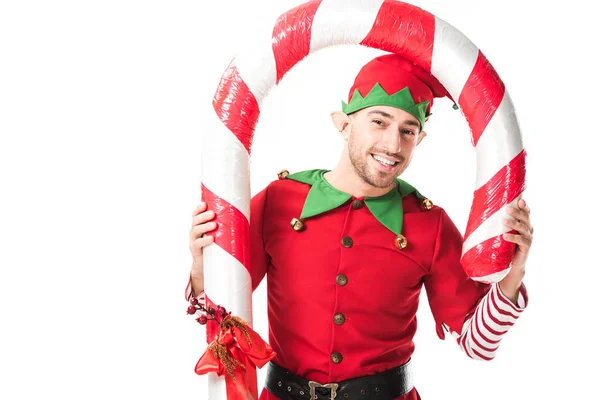 Homme souriant en costume d'elfe de Noël debout sous une grosse canne à bonbons isolé sur blanc — Photo de stock