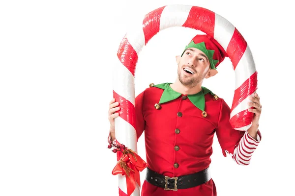 Homme heureux en costume d'elfe de Noël debout sous la grosse canne à bonbons isolé sur blanc — Photo de stock