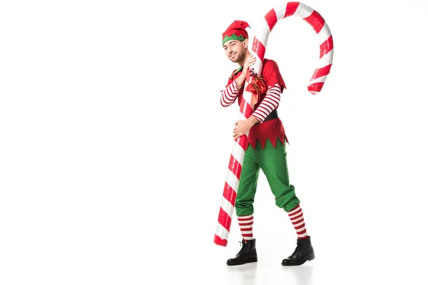 Man in christmas elf costume carrying big candy cane isolated on white — Stock Photo