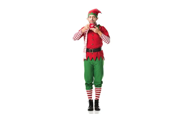 Uomo in costume elfo di Natale con gli occhi chiusi in possesso di tazza di tè e aroma inalatorio isolato su bianco — Foto stock