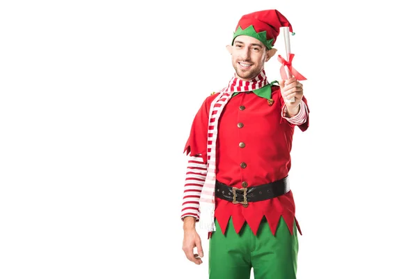 Sonriente hombre en traje de elfo de Navidad sosteniendo lista de deseos rollo y mirando a la cámara aislada en blanco - foto de stock