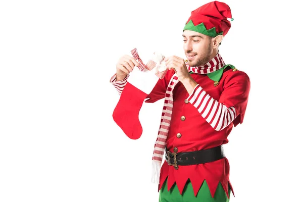 Hombre en traje de elfo de Navidad poniendo presente en medias de Navidad roja aislado en blanco - foto de stock