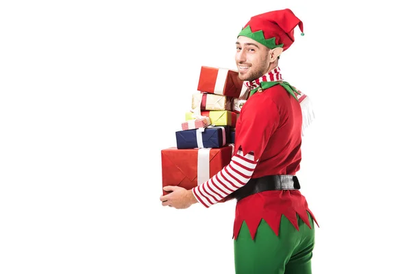 Усміхнений чоловік у різдвяному ельфійському костюмі дивиться на камеру і несе купу подарунків ізольовано на білому — стокове фото