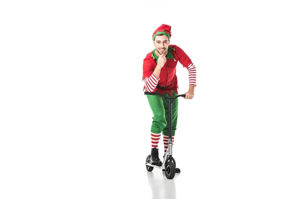 Hombre feliz en traje de elfo de Navidad tocando la barbilla y montar en bicicleta de empuje aislado en blanco - foto de stock