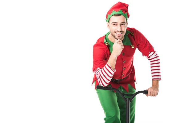 Homme souriant en costume d'elfe de Noël regardant la caméra, toucher le menton et équitation push-cycle isolé sur blanc — Photo de stock