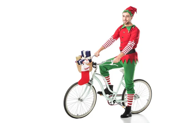 Чоловік у різдвяному ельфійському костюмі їзда на велосипеді з кошиком, повним подарунків ізольовано на білому — стокове фото