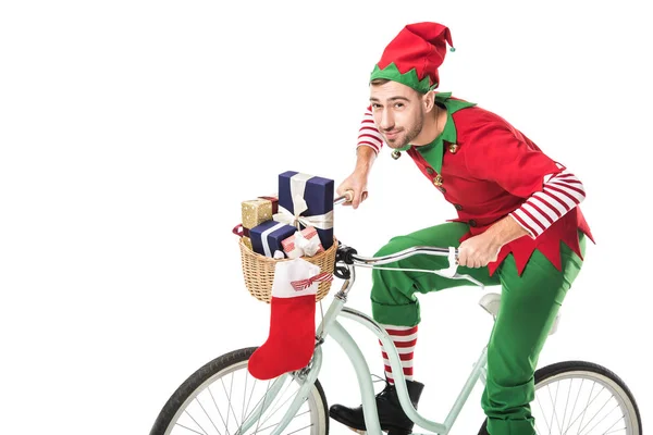 Homme souriant en costume d'elfe de Noël équitation vélo et le transport de cadeaux dans le panier isolé sur fond blanc — Photo de stock