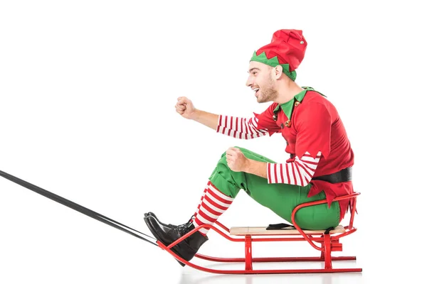 Aufgeregter glücklicher Mann im Weihnachtselfenkostüm, der Schlitten fährt, isoliert auf weißem Grund — Stockfoto