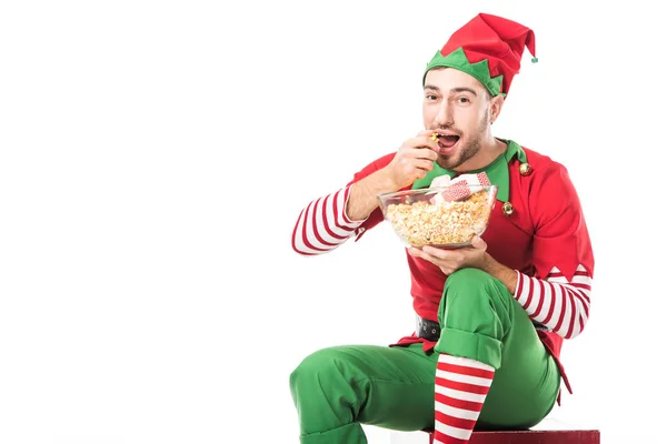 Hombre en traje de elfo de Navidad comiendo palomitas de maíz y mirando a la cámara aislada en blanco - foto de stock
