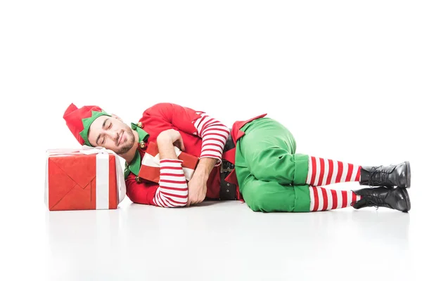 Man in christmas elf costume sleeping on pile of presents isolated on white — Stock Photo