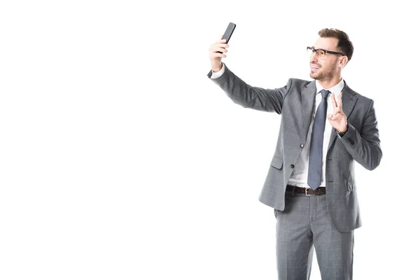Sorridente uomo d'affari adulto prendendo selfie e mostrando segno di pace isolato su bianco — Foto stock