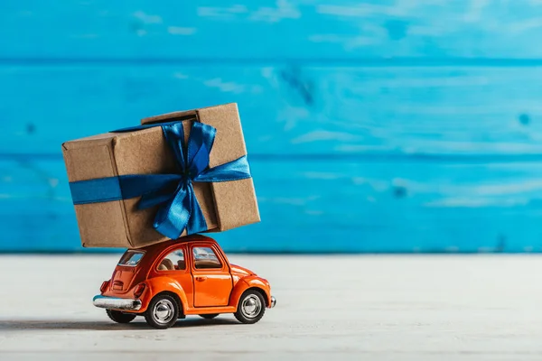 Close-up shot of toy car with gift box on blue wooden background — Stock Photo