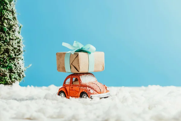 Close-up shot of toy red car with christmas gift box riding by snow made of cotton on blue background — Stock Photo