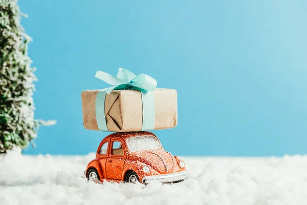 Close-up shot of toy car with christmas gift box riding by snow made of cotton on blue background — Stock Photo