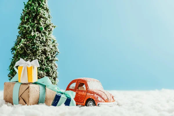 Крупним планом знімок іграшкового червоного автомобіля з подарунками та ялинкою, що стоїть на снігу з бавовни на синьому фоні — стокове фото