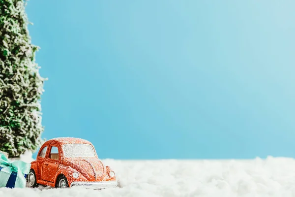 Gros plan de la voiture jouet avec des cadeaux et arbre de Noël debout sur la neige en coton sur fond bleu — Photo de stock