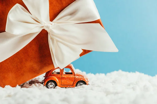 Side view of toy vehicle and big christmas gift riding by snow made of cotton on blue background — Stock Photo