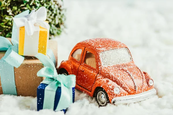 Gros plan de la voiture jouet avec des cadeaux et arbre de Noël debout sur la neige en coton — Photo de stock