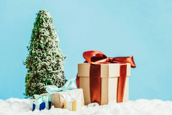 Close-up shot of christmas gifts and miniature christmas tree standing on snow on blue background — Stock Photo