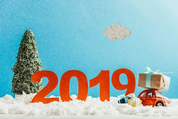 Big red 2019 numbers with toy car, gifts and christmas tree on snow for new year — Stock Photo