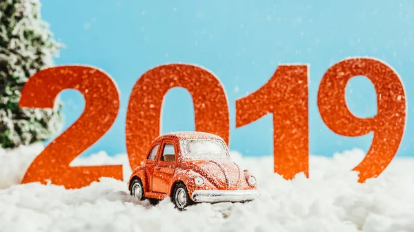 Великі червоні номери 2019 року з іграшковим автомобілем, що стоїть на снігу на синьому фоні, концепція нового року — стокове фото