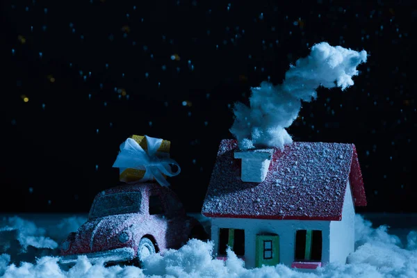 Gros plan de voiture jouet avec cadeaux de Noël et maison couverte de neige dans la nuit — Photo de stock