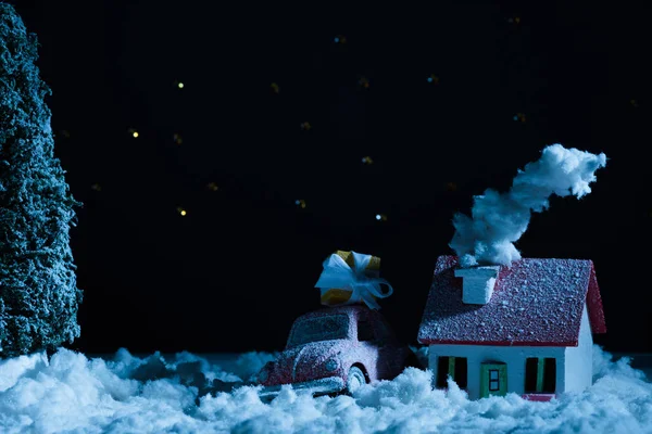 Primo piano di macchina giocattolo con regalo di Natale e casa coperta di neve nella notte — Foto stock