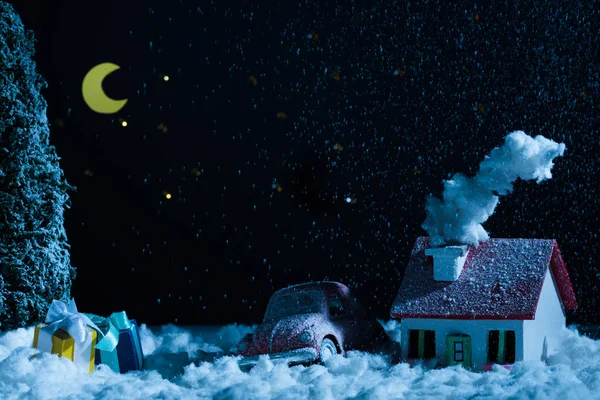 Close-up shot of toy car with christmas gifts and house covered with snow in night — Stock Photo