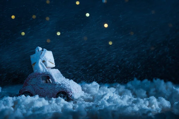 Primo piano di auto giocattolo con scatola regalo in piedi nella neve durante la notte sotto il cielo stellato, concetto di Natale — Foto stock