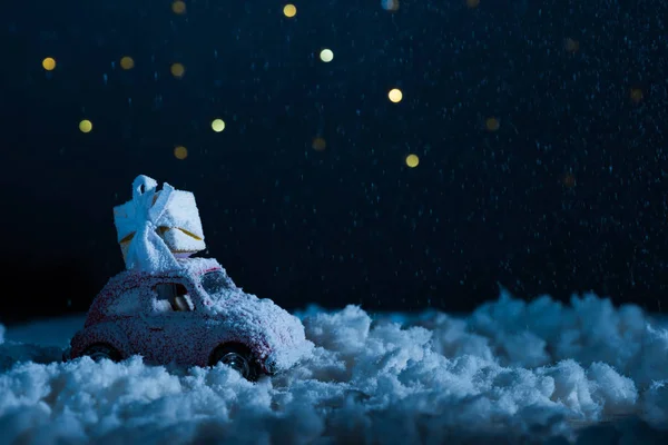 Gros plan de voiture jouet avec boîte cadeau debout dans la neige dans la nuit, concept de Noël — Photo de stock