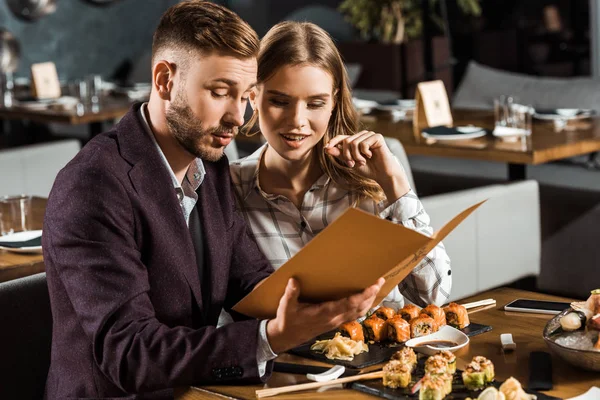 Schönes junges erwachsenes Paar sucht in Speisekarte, um Abendessen im Restaurant zu bestellen — Stockfoto