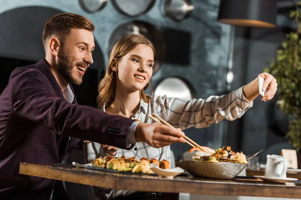 Hermosa pareja de jóvenes adultos tomando selfie mientras cenan en el restaurante - foto de stock