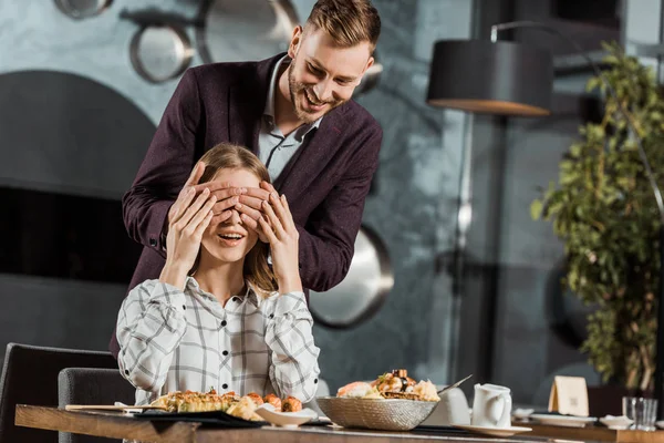 Schöner Mann schließt Augen seiner Freundin, um im Restaurant für eine Überraschung zu sorgen — Stockfoto