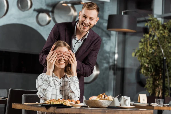 Bonito homem fechando os olhos de sua namorada para fazer surpresa no restaurante — Fotografia de Stock