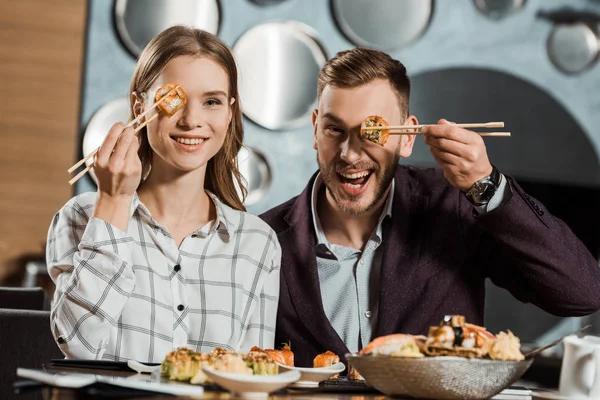 Lovely couple having fun while eating sushi rolls in restaurant — Stock Photo