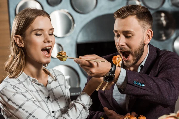 Beautiful couple of young adult feeding each other with sushi in restaurant — Stock Photo
