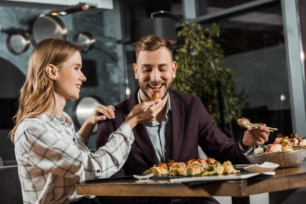 Attractive young adult woman feeding her handsome boyfriend in restaurant — Stock Photo