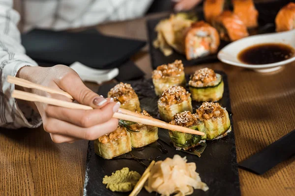 Vista parcial da mulher comendo rolos de sushi com pauzinhos — Fotografia de Stock