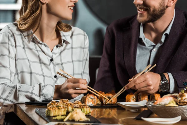 Vista parcial de una pareja sonriente comiendo sushi en el restaurante - foto de stock