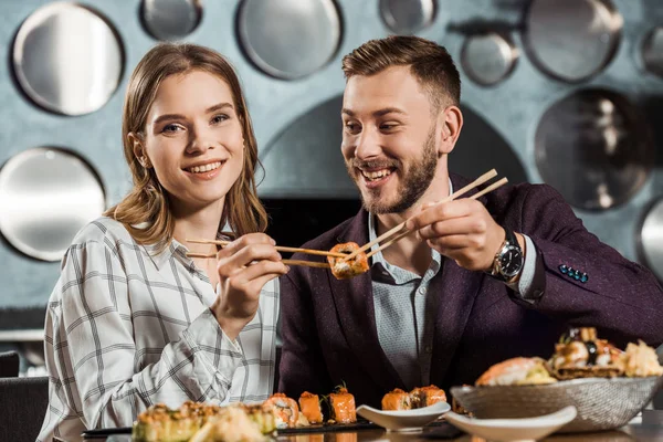 Feliz pareja de jóvenes adultos comiendo sushi en el restaurante - foto de stock