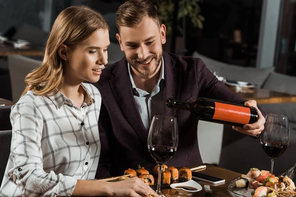 Bonito homem derramando vinho em copos enquanto casal jantando no restaurante — Fotografia de Stock