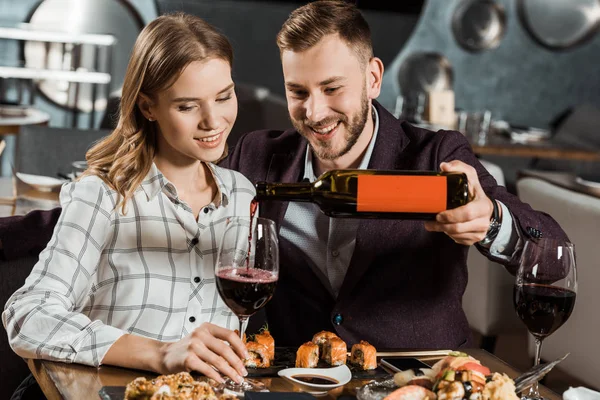 Привлекательная пара ужинает, пока мужчина наливает вино в бокалы в ресторане — стоковое фото