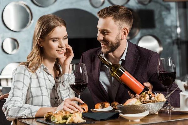 Bonito homem oferecendo sua bela namorada vinho enquanto jantam no restaurante — Fotografia de Stock