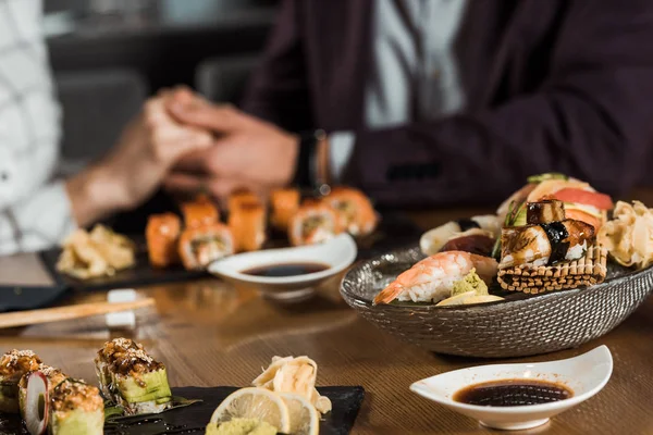 Rollos de sushi y mariscos en el fondo de la pareja tomados de la mano - foto de stock
