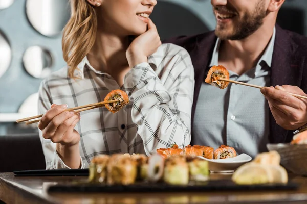 Vista recortada de la feliz pareja sonriente comiendo sushi en el restaurante - foto de stock