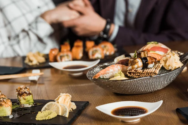 Rollos de sushi y mariscos en el fondo de la pareja tomados de la mano — Stock Photo